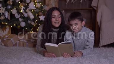 在圣诞节，妈妈给儿子读了一本书，吻了他躺在圣诞树附近的地板上。 高清高清